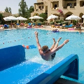A man enjoying the pool while sliding down a waterslide into the water. He appears excited and immersed in the fun experience.