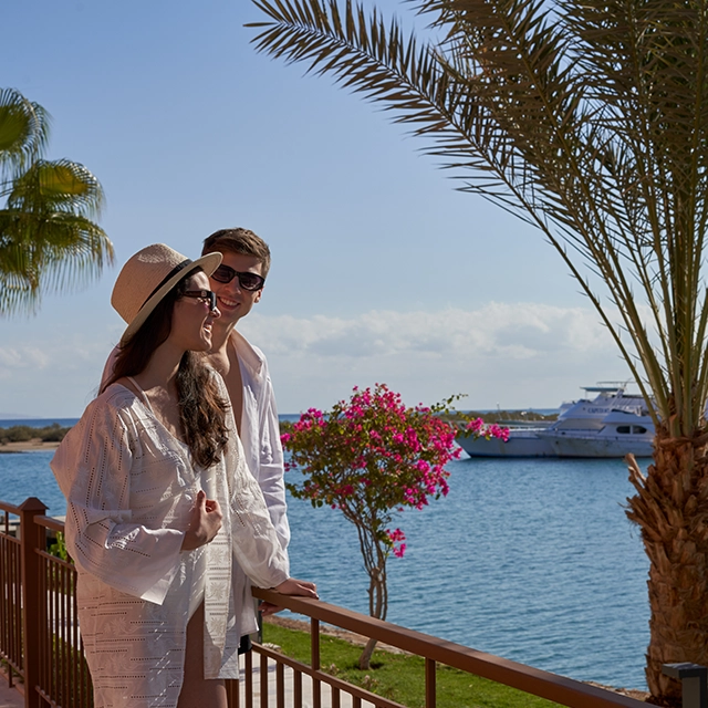 A couple shares a romantic moment framed by the expansive sea and a luxurious yacht in the background, capturing the essence of serene beauty and tranquility.