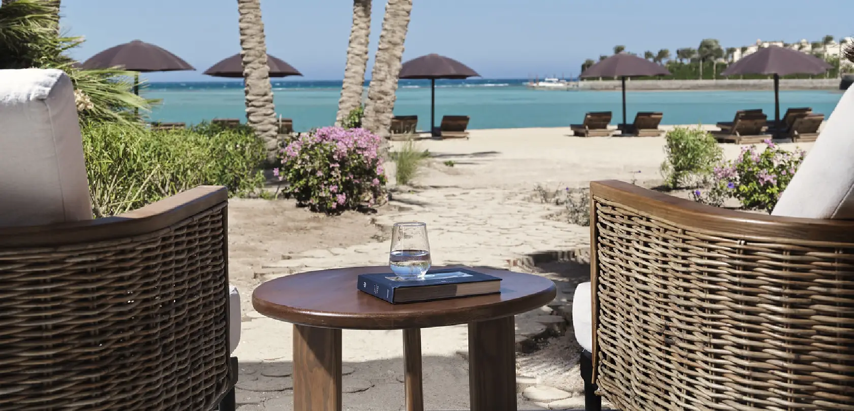 Seaside sitting area on the beach with comfortable chairs and tables, overlooking the sea and clear blue sky.