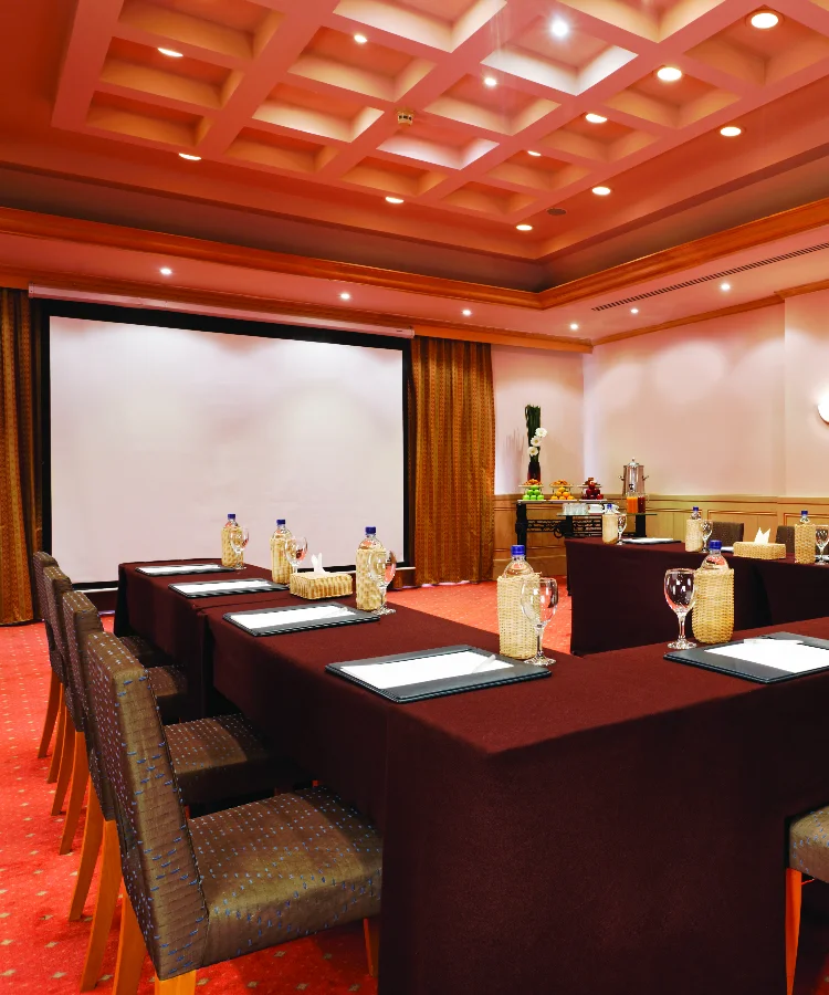 A meeting room at Mövenpick Hotel El Gouna with a large table, chairs, and a projector screen.
