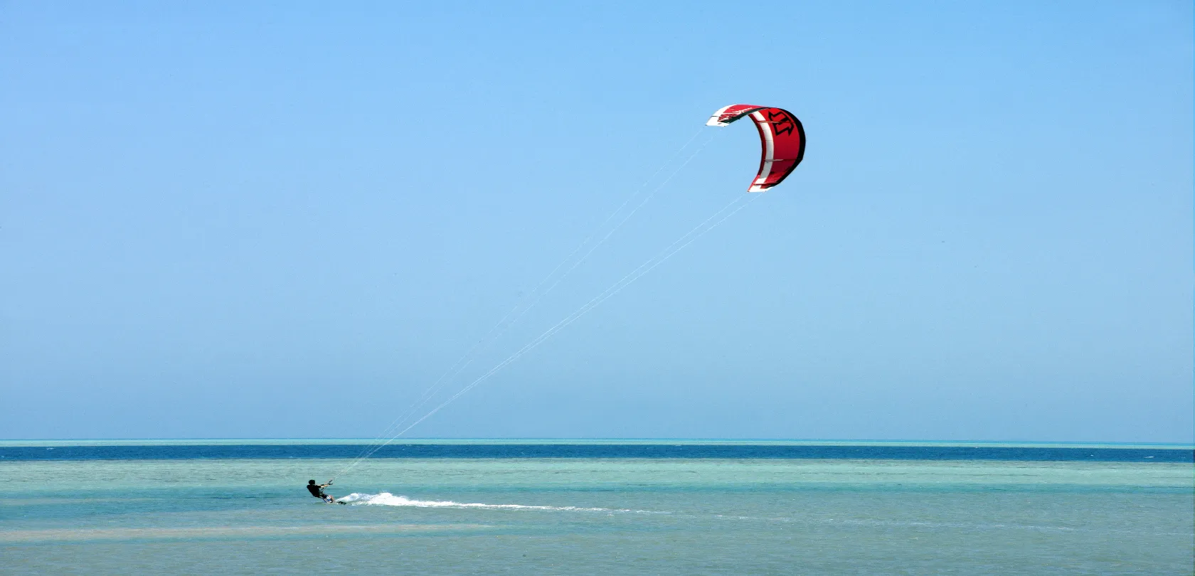Person kite surfing on a windy day, gliding over waves in the sea with a colorful kite flying above.