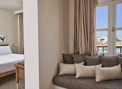 Junior suite sitting area at Captains Inn, El Gouna, Red Sea, Egypt. The space features comfortable seating with plush sofas and armchairs, arranged around a coffee table. The decor is elegant and modern, with neutral tones and stylish accents. Large windows allow natural light to brighten the area, creating a welcoming and relaxing atmosphere. The sitting area is designed for both comfort and sophistication, providing a perfect spot for guests to unwind.