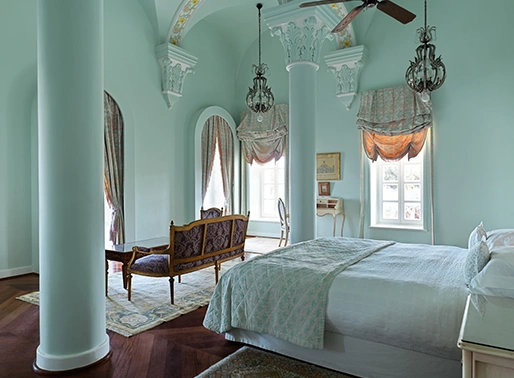 Elegant room at La Maison Bleue featuring classic décor, a plush king-size bed, antique furnishings, and a large window offering a picturesque view of the surrounding landscape, filling the room with natural light.