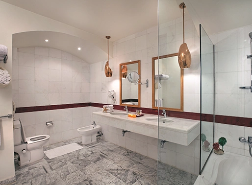 The bathroom of a deluxe suite at Moevenpick, featuring luxurious and modern amenities. The space includes a large, freestanding bathtub, a walk-in shower with glass doors, and a double vanity with sleek sinks. The decor is elegant with high-end finishes, including marble countertops and polished fixtures, creating a sophisticated and relaxing environment.