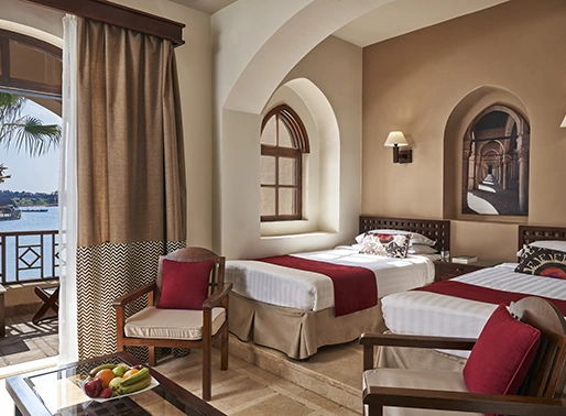 Twin bedroom with a lagoon view, featuring a red-themed decor. The room includes two twin beds with bold red accents, stylish furnishings, and large windows showcasing the lagoon view. The space is designed with a vibrant color palette, offering a lively and inviting atmosphere.